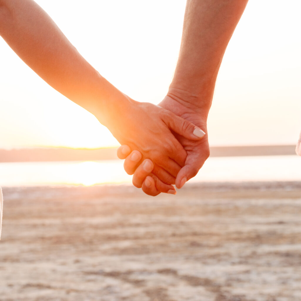 Close up of a couple holding hands at the beach